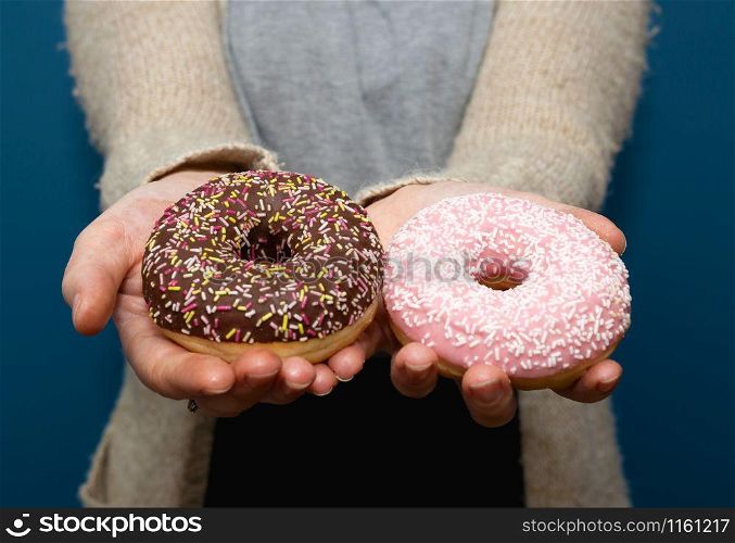 Woman holding a delicious colorful donut with sprinkles and giving the donut away, sharing near blue background. Woman holding a delicious colorful donut with sprinkles and giving the donut away, sharing