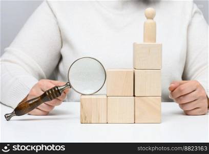 Woman holding a magnifying glass and wooden men on a white table. Personnel recruitment concept, talented employees. Career advancement