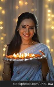 Woman holding a plate full of diyas in her hand and smiling