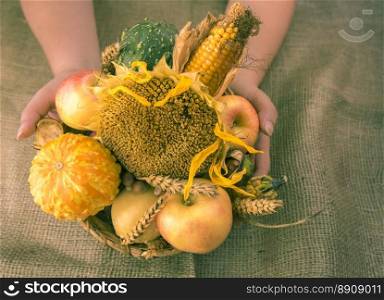 Woman holding a round wicker basket full with autumn products, such as pumpkins, sunflower, corn, apples, grain and more