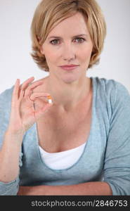 Woman holding a small orange and white capsule of medicine