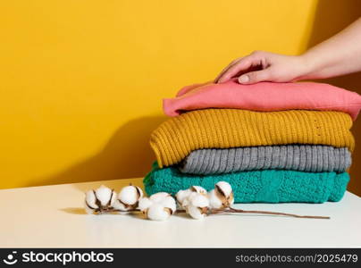 woman holding a stack of knitted folded sweaters on a yellow background. Washing clothes, cleaning things