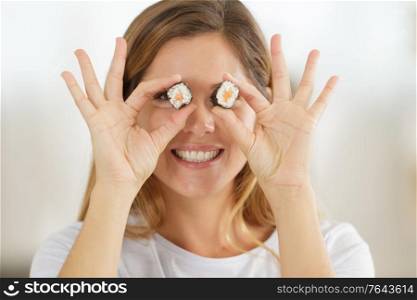 woman holding a suchi roll in front of each eye