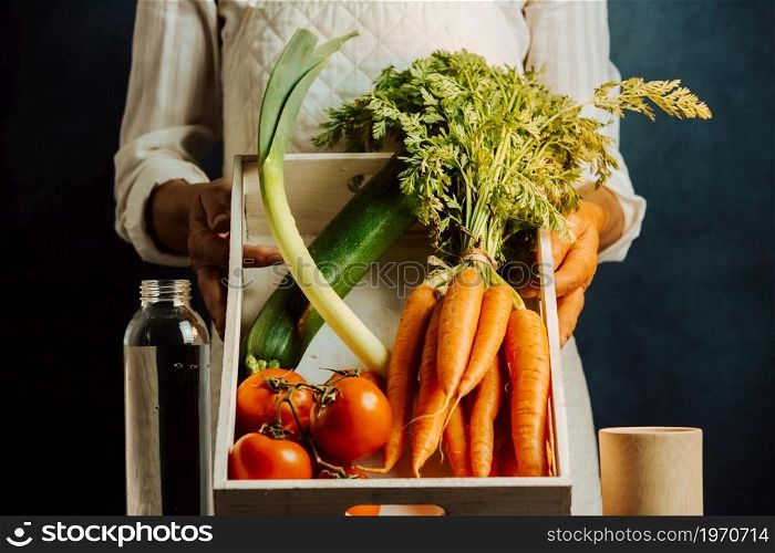 Woman holding a white box of vegetables over a table with water near her, healthy food concept with copy space