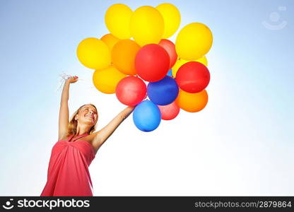 Woman holding balloons against sun and sky