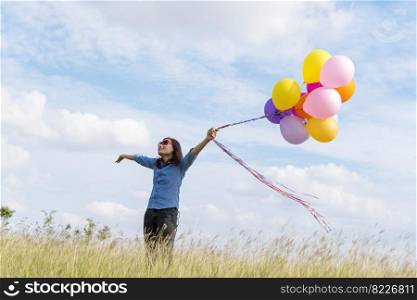 Woman holding balloons running on green meadow white cloud and blue sky with happiness Cheerful and relax. Hands holding vibrant air balloons play on birthday party happy times summer sunlight outdoor