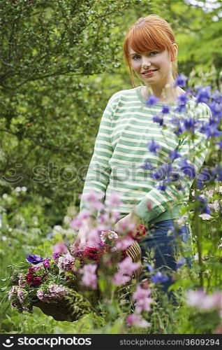Woman holding basket of flowers in garden, portrait
