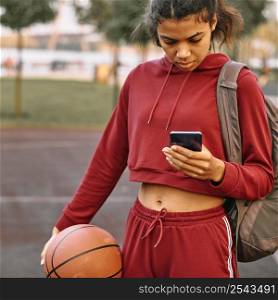 woman holding basketball outdoors checking her phone 2