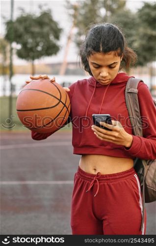 woman holding basketball while checking her phone
