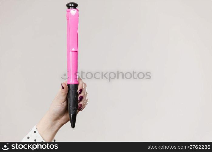 Woman holding big oversized pen. Studio shot on light background with copyspace.. Woman holding big oversized pen
