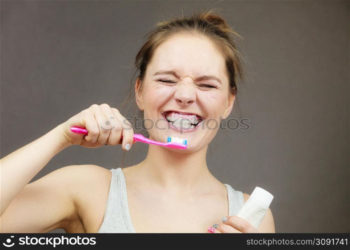 Woman holding brush and tooth paste for teeth cleaning. Happy funny smiling girl with toothbrush. Oral hygiene. Studio shot dark background. Woman brushing cleaning teeth