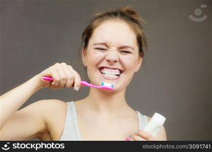 Woman holding brush and tooth paste for teeth cleaning. Happy funny smiling girl with toothbrush. Oral hygiene. Studio shot dark background. Woman brushing cleaning teeth