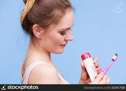 Woman holding brush and tooth paste for teeth cleaning. Happy smiling girl with toothbrush. Oral hygiene. Studio shot blue background. Woman holds toothbrush and paste for teeth cleaning