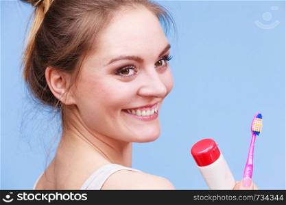 Woman holding brush and tooth paste for teeth cleaning. Happy smiling girl with toothbrush. Oral hygiene. Studio shot blue background. Woman holds toothbrush and paste for teeth cleaning