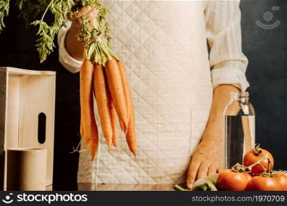 Woman holding carrots and vegetables over a table with water near her, healthy food concept with copy space