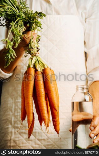 Woman holding carrots and vegetables over a table with water near her, healthy food concept with copy space