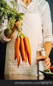 Woman holding carrots and vegetables over a table with water near her, healthy food concept with copy space