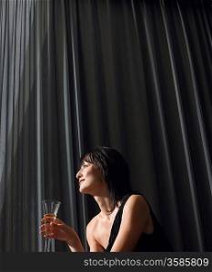 Woman holding champagne in front of curtains indoors