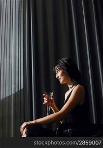 Woman holding champagne in front of curtains indoors side view