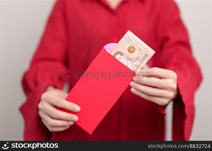 Woman holding Chinese red envelope with Thai baht money gift for happy Lunar New Year holiday