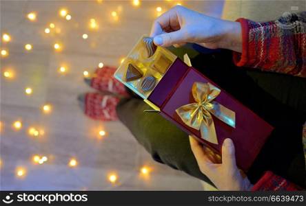 Woman Holding Chocolate Present Next To Christmas Lights