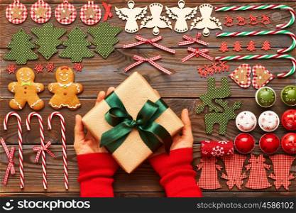 Woman holding christmas present over wooden background with homemade gingerbread cookie and handmade decoration on it