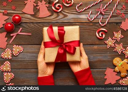 Woman holding christmas present over wooden background with homemade gingerbread cookie and handmade decoration on it