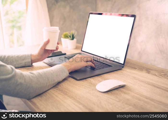 Woman holding coffee and using laptop on wooden table in office