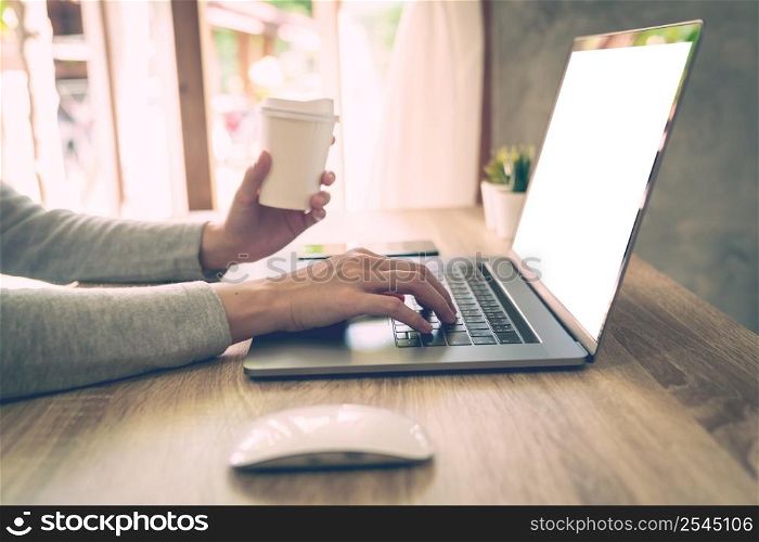 Woman holding coffee and using laptop on wooden table in office