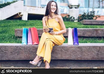 woman holding coffee cup & smartphone with shopping bags. shopaholic consumerism lifestyle in mall