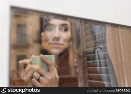 woman holding cup coffee while looking outdoors