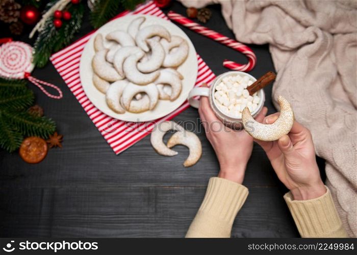 Woman holding cup of cocoa with marshmallow and Vanillekipferl vanilla kipferl cookies on a plate. High quality photo. Woman holding cup of cocoa with marshmallow and Vanillekipferl vanilla kipferl cookies on a plate