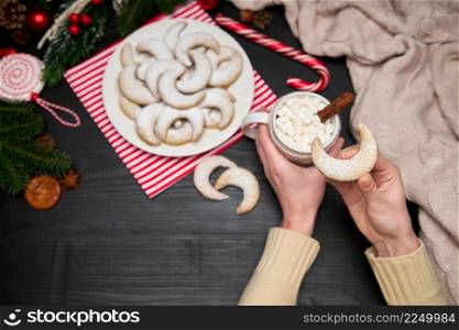Woman holding cup of cocoa with marshmallow and Vanillekipferl vanilla kipferl cookies on a plate. High quality photo. Woman holding cup of cocoa with marshmallow and Vanillekipferl vanilla kipferl cookies on a plate