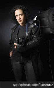 Woman holding digital camera in studio setting.