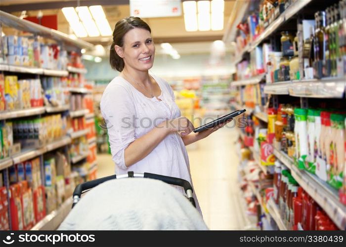 Woman holding digital tablet with baby stroller in foreground while looking at camera in shopping centre
