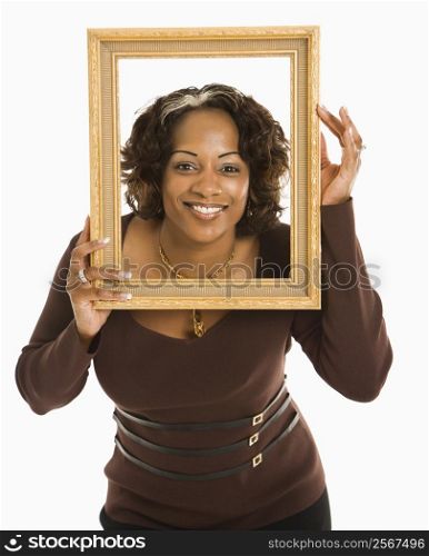 Woman holding empty frame around head smiling.