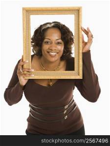Woman holding empty frame around head smiling.