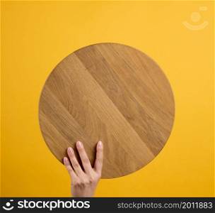 woman holding empty round wooden pizza board in hand, body part on a yellow background