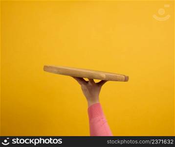 woman holding empty round wooden pizza board in hand, body part on a yellow background