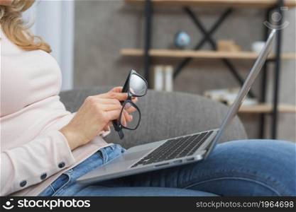 woman holding eyeglasses hand sitting sofa with open laptop her lap. High resolution photo. woman holding eyeglasses hand sitting sofa with open laptop her lap. High quality photo