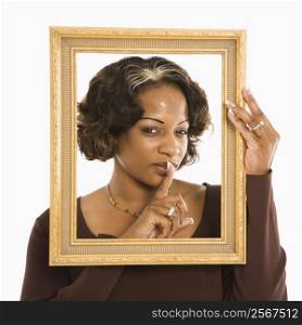 Woman holding frame around head holding finger up to lips.