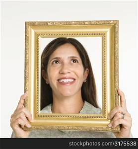 Woman holding frame in front of face smiling.