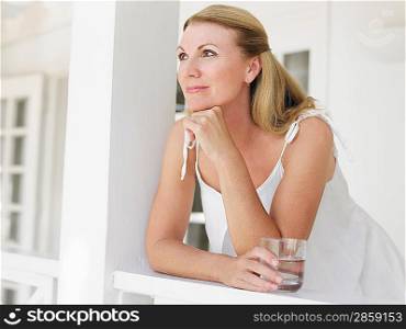 Woman holding glass of water leaning on verandah balustrade portrait