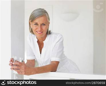 Woman holding glass of water leaning on verandah balustrade portrait