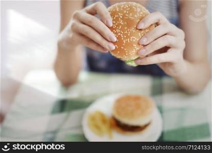 Woman holding hamburger and sitting at the table