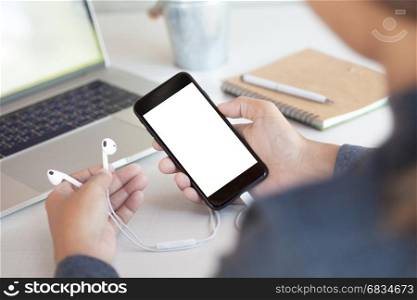 woman holding headphone and phone white screen on table third person view