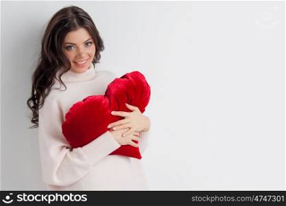 Woman holding heart pillow. Beautiful woman in casual sweater holding red heart shaped pillow