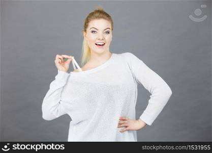 Woman holding her bra strap from under her sweater. Brafitting concept. Grey background.. Woman holding her bra strap