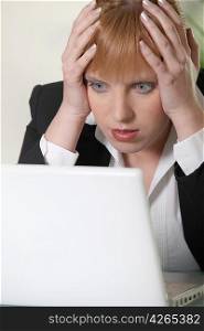 Woman holding her head in shock as she looks at a laptop computer
