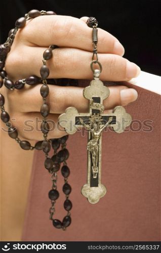 Woman holding Holy Bible open with rosary and crucifix in hand.